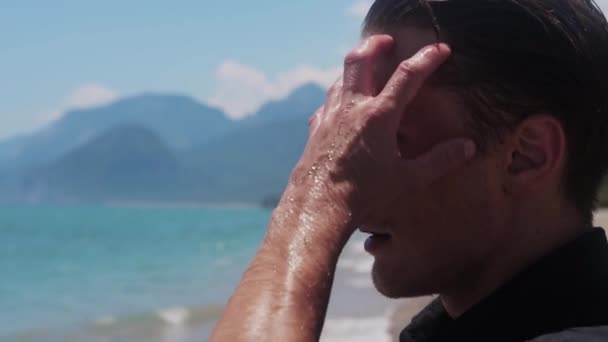 Un hombre atractivo peina el cabello mojado junto al mar. Mid shot - Metraje, vídeo