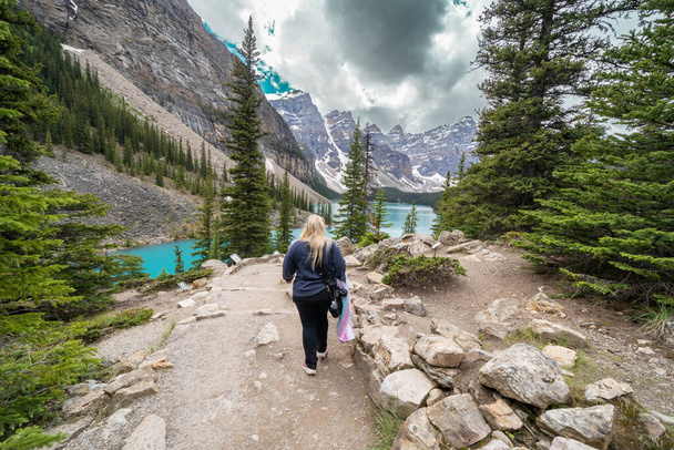 A kamerát szállító nő a Moraine tónál sétál a Rockpile ösvényen a Banff Nemzeti Parkban. - Fotó, kép