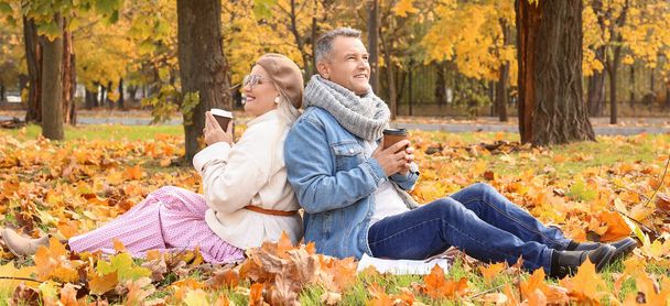 Happy mature couple drinking coffee in autumn park - Foto, imagen