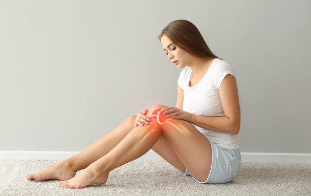 Woman with pain in knee on light background - Φωτογραφία, εικόνα