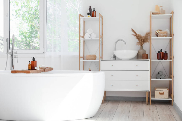 Interior elegante do banheiro com banheira moderna e unidades de prateleira com acessórios de banho - Foto, Imagem