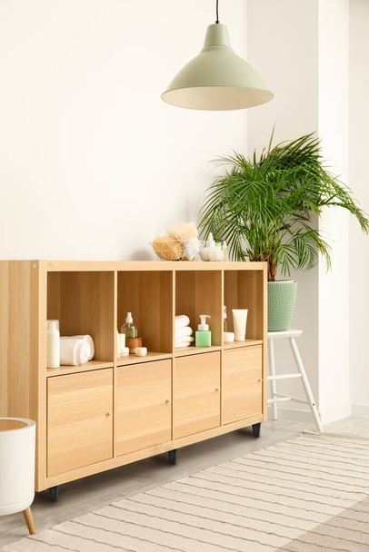 Shelf unit with different bath accessories and houseplant near white wall in bathroom interior - Foto, Bild
