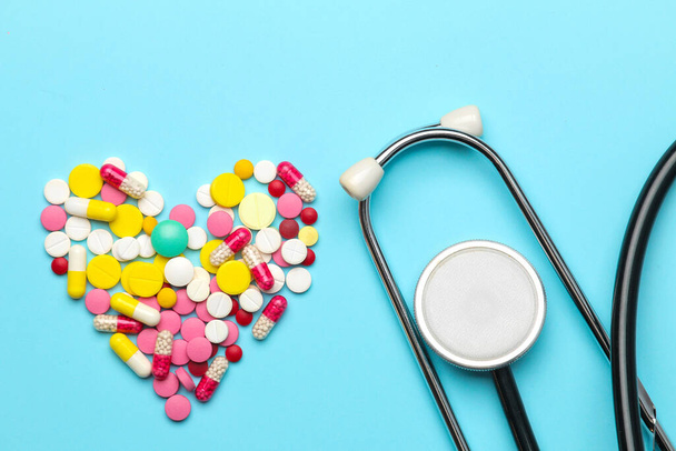 Various heart shaped pills and a stethoscope on a blue background. top view and free space. Cardiology and treatment of heart disease. - Foto, imagen