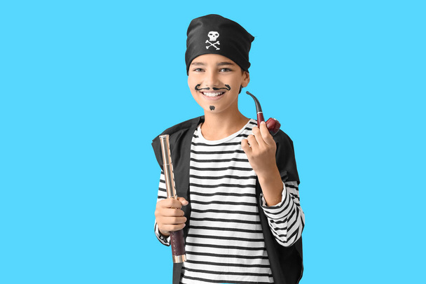 Malý chlapec oblečený jako pirát s dalekohledem a kouřící dýmkou na modrém pozadí - Fotografie, Obrázek