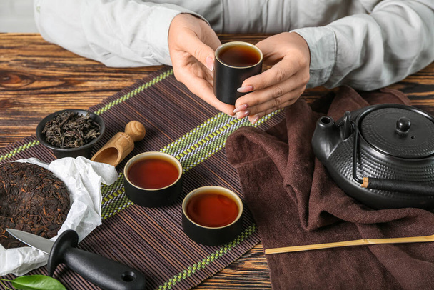Woman with cup of puer tea at wooden table, closeup - Фото, изображение
