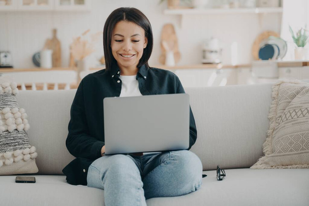 Boldog európai lány gépel a számítógépen. Üzletasszony dolgozik startup projekt otthonról. Lady szabadúszó ül kényelmes kanapén laptoppal és mosolyog, nézi a képernyőn. - Fotó, kép