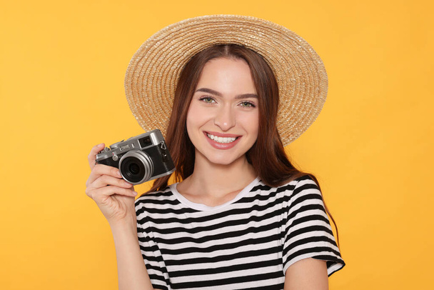 Young woman with camera on yellow background. Interesting hobby - Φωτογραφία, εικόνα