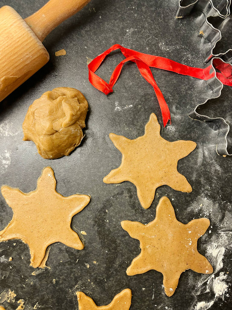Baking Christmas cookies. Raw gingerbread dough on kitchen table. Some of the dough is star shaped. Concept of festive homemade baking for the christmas celebrations. - Fotografie, Obrázek