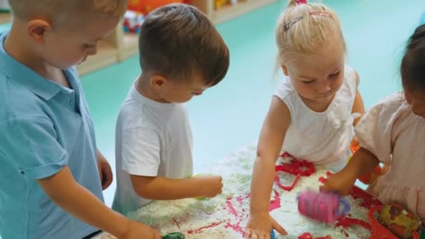 Sensory play at nursery school. Toddlers with their teacher having fun with white, fluffy cloud dough, and using modeling tools such as colorful and textured rolling pins, cutters, silicone shape - Video