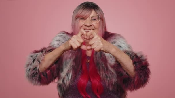 Woman in love. Smiling stylish old woman makes heart gesture demonstrates love sign expresses good feelings and sympathy. Senior elderly grandmother 70s isolated alone on pink studio wall background - Footage, Video