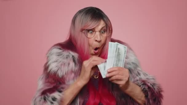 Богатая довольна босс стильная женщина размахивает деньгами доллар наличные банкноты векселя, как вентилятор, успешной бизнес-карьеры, победитель лотереи, большой доход, богатство. Старшая бабушка изолирована на розовом фоне студии - Кадры, видео