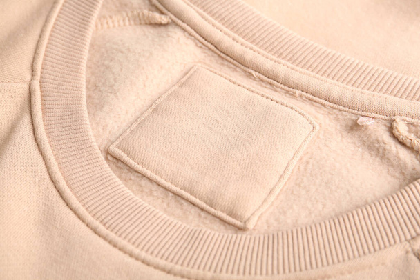 Blank clothing label on beige sweater, closeup - Fotó, kép
