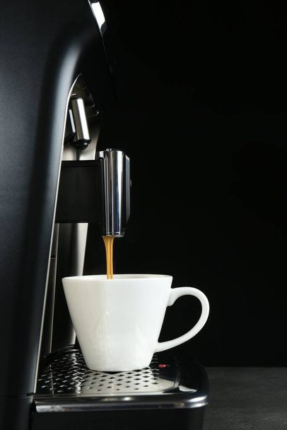 Modern espresso machine pouring coffee into cup on grey table against black background - Φωτογραφία, εικόνα