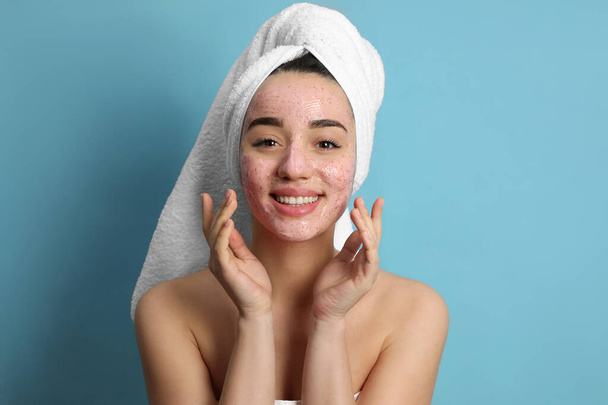 Woman applying pomegranate face mask on light blue background - Foto, afbeelding