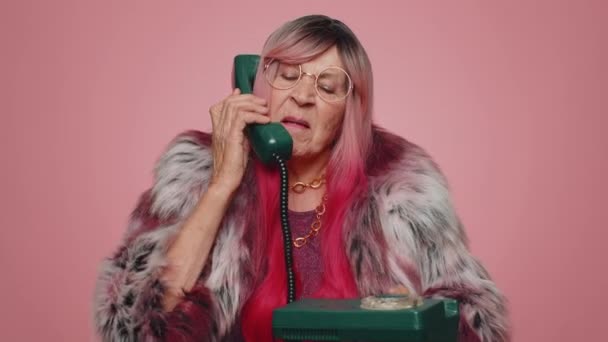 Божевільна туристична хакерка літня жінка розмовляє по дротовому старовинному телефону 80-х років, обманюючи, створюючи дурні обличчя. Старша стильна бабуся бабуся гарячої лінії агент ізольовані один на рожевому студійному фоні
 - Кадри, відео