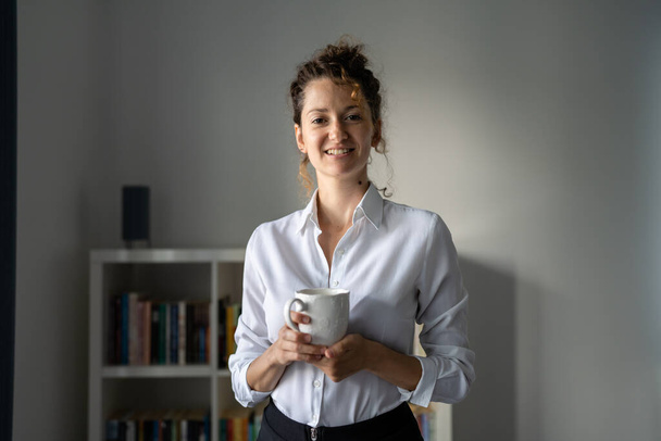 Одна деловая женщина молодая взрослая белая женщина, стоящая в офисе утренняя рутина уверенная счастливая улыбка с чашкой кофе копировальное пространство - Фото, изображение