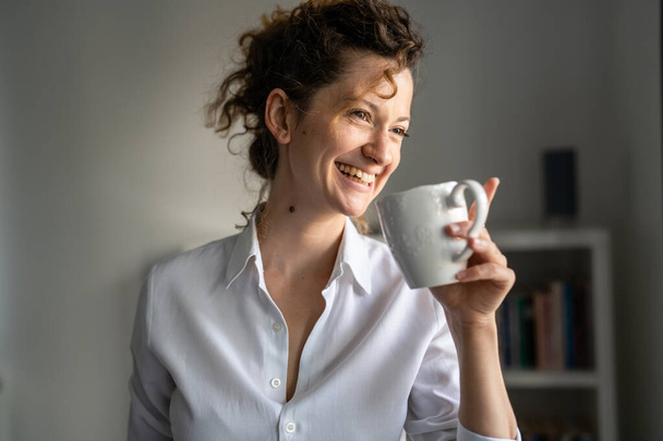 One business woman young adult female caucasian standing in the office morning routine confident happy smile with cup of coffee copy space - Foto, Imagem