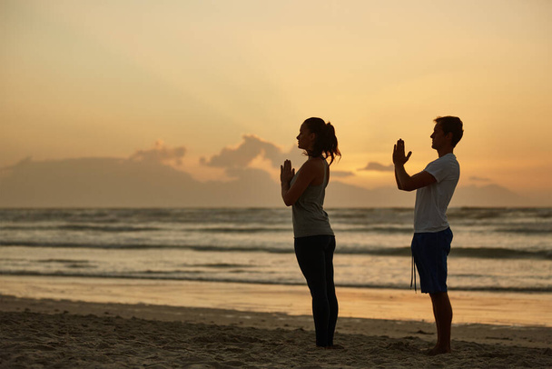Profiter de la paix et de la tranquillité de la nature. un couple faisant du yoga sur la plage au coucher du soleil - Photo, image