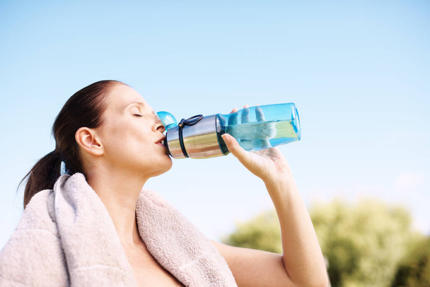 Refresca como nada en la tierra. Una mujer atractiva bebiendo de su botella de agua después de un entrenamiento - Foto, imagen
