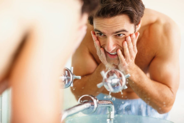 Щасливий молодий хлопець миє обличчя в умивальнику. Усміхнений молодий чоловік миє обличчя у ванній
 - Фото, зображення