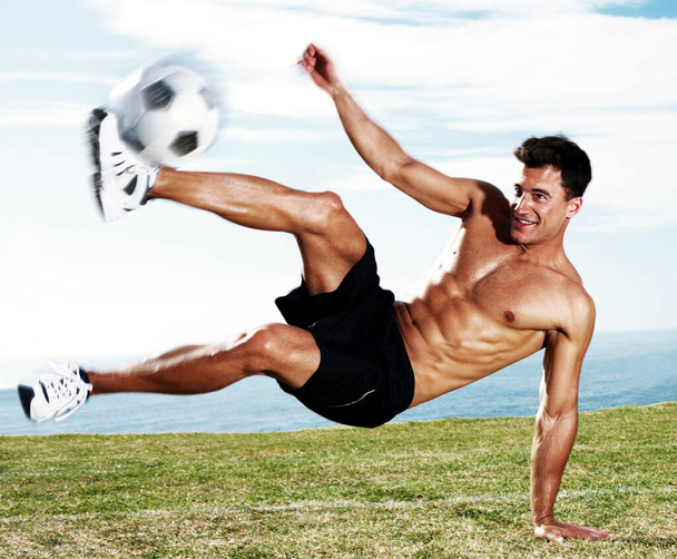 Νεαρός ποδοσφαιριστής κλωτσάει το ποδόσφαιρο εν δράσει. Πορτρέτο ενός νεαρού ποδοσφαιριστή κλοτσιές το ποδόσφαιρο σε δράση κατά του ουρανού - Φωτογραφία, εικόνα