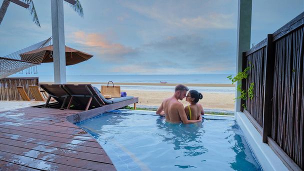 豪華な休暇中の日没の間に海とビーチを見下ろすプランジプールで楽しむ豪華なヴィラでカップル。休暇中の男性と女性日没を見て - 写真・画像