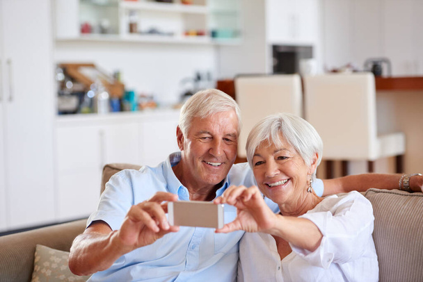 Envoyons celui-ci à nos enfants. un couple de personnes âgées prenant un selfie avec leur téléphone portable assis sur le canapé - Photo, image