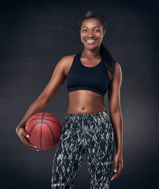 Lets play some basketball. Studio shot of a beautiful young woman holding a basketball against a black background - Foto, imagen