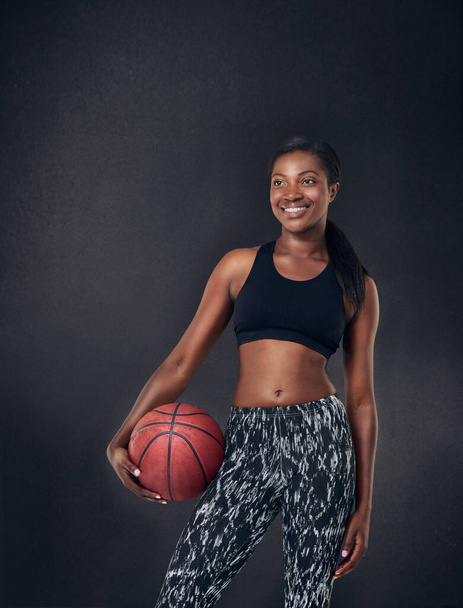Fit is the only option. Studio shot of a beautiful young woman holding a basketball against a black background - Foto, afbeelding