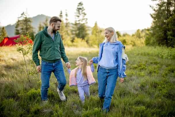 Young caucasian couple with little girl walk together while traveling in the mountains. Happy family spending summer vacation on nature - Photo, Image