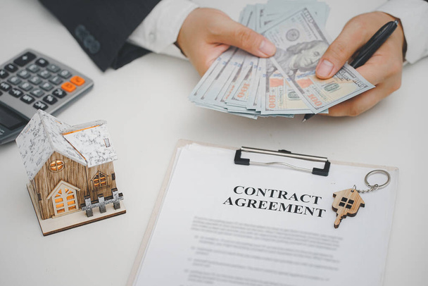 Real estate agent with cash money ,model house , house key and contract agreement on desk. real estate, home loan and investments concept - 写真・画像