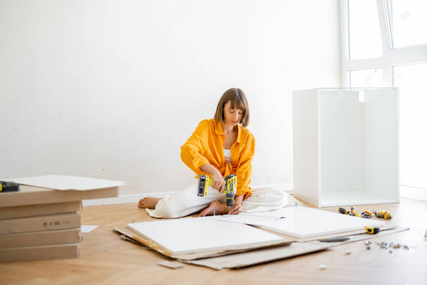 Young woman assembles furniture by herself while renovating her new apartment. DIY and house improvement concept - 写真・画像