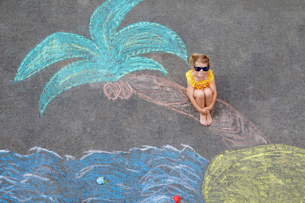 Happy little preschool girl in swimsuit with sea, sand, palm painted with colorful chalks on asphalt. Cute child with having fun with chalk picture. Summer, vacations, summertime. - Foto, immagini