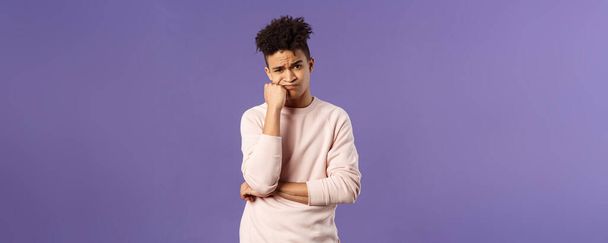 Portrait of complicated, troubled young hispanic man facing tough problem, lean on fist grimacing and pouting, solving troublesome situation, thinking, feeling uneasy, purple background. - Foto, Bild