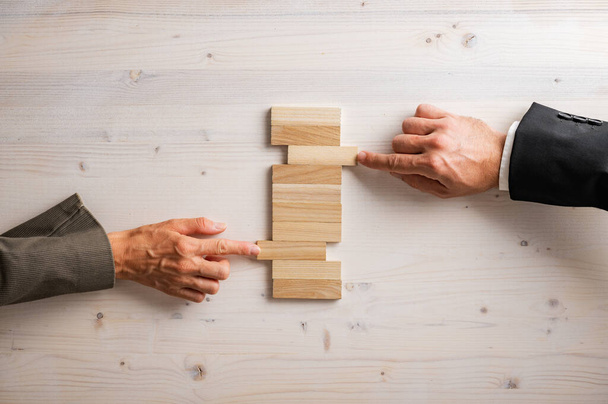 Hands of businessman and businesswoman pushing two blank  wooden pegs into a stack of them in a conceptual image of partnership and cooperation. - Photo, Image