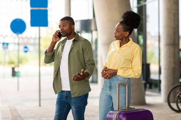 旅行通信の問題。空港近くのスーツケースで立ち上がる問題を抱えている電話で話す不幸な黒人観光客カップルターミナル外。観光と交通のトラブル - 写真・画像