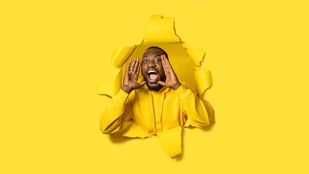 Astonished shouting. Emotional black man in torn yellow paper background, screaming, holding hands near mouth. Concept of human emotions, facial expression, sales, ad. - Fotografie, Obrázek