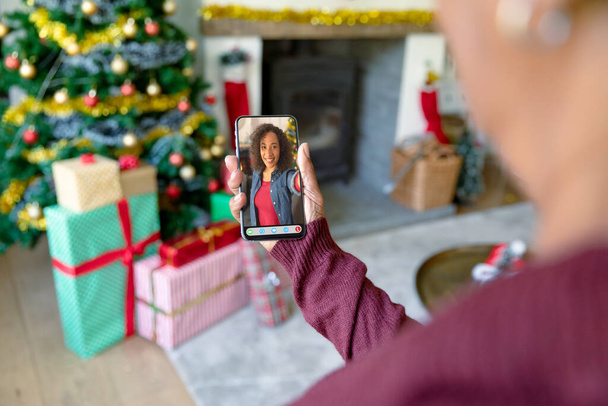 Woman making smartphone christmas video call with smiling african american woman. christmas, festivity and communication technology. - Φωτογραφία, εικόνα