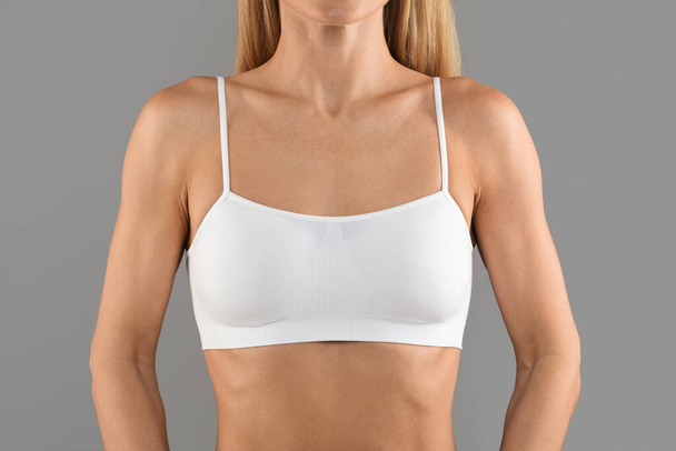 Front View Of Young Female Wearing White Top Bra Standing Isolated Over Grey Background In Studio, Cropped Shot Of Unrecognizable Slim Woman In Sport Style Underwear, Closeup - Foto, immagini