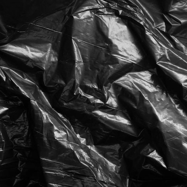Reflecting light and shadow on creases and folds in black plastic sheeting. monochrome light and texture, abstract background image. - Valokuva, kuva