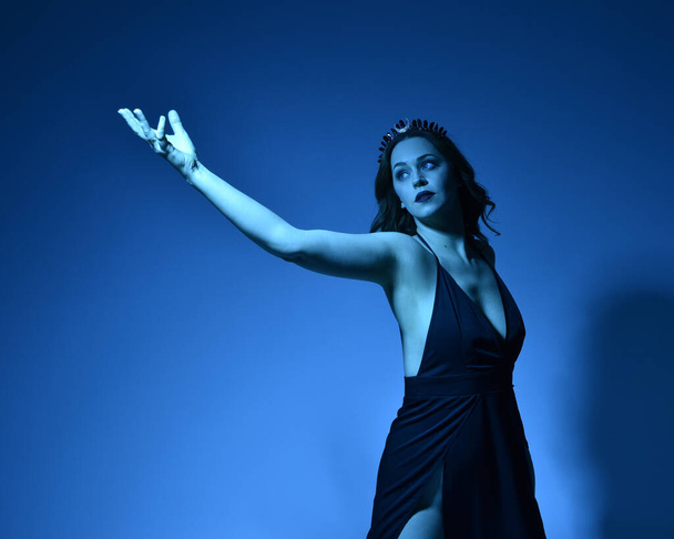 Close up portret pięknej modelki w eleganckiej czarnej sukience i koronie, pozowanie na tle studio z fantazji inspirowane gesty ramienia, wielokolorowe kreatywne oświetlenie. - Zdjęcie, obraz