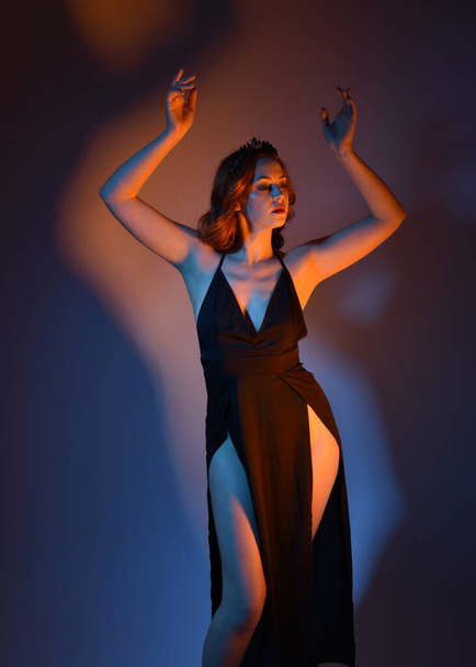 Nahaufnahme Porträt der schönen Frau Modell trägt elegante schwarze Kleid, posiert vor einem Studio-Hintergrund mit Fantasie inspirierten Armgesten, mehrfarbige kreative Beleuchtung. - Foto, Bild