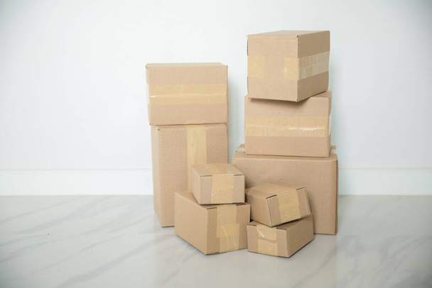 Stack of cardboard boxes for moving, Empty room with a white wall and cardboard boxes with unbranded barcode on the floor. Delivery of goods, shopping. Cardboard boxes on gray wall background. - Photo, image