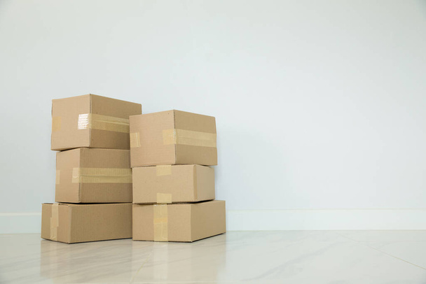 Stack of cardboard boxes for moving, Empty room with a white wall and cardboard boxes with unbranded barcode on the floor. Delivery of goods, shopping. Cardboard boxes on gray wall background. - Photo, image
