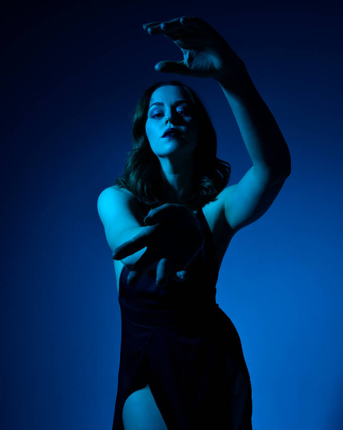 Close-up portret van mooie vrouw model dragen elegante zwarte jurk, poseren tegen een studio achtergrond met fantasie geïnspireerde arm gebaren, multi gekleurde creatieve verlichting. - Foto, afbeelding