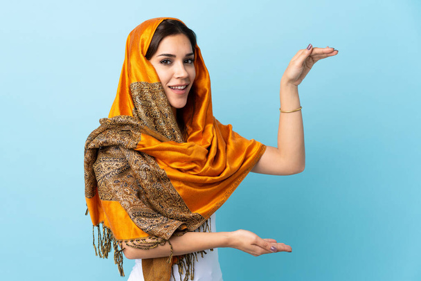 青の背景に隔離された伝統的な衣装を持つ若いモロッコの女性は、広告を挿入するためのコピースペースを保持 - 写真・画像