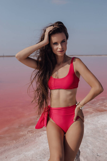 fashion outdoor photo photo of beautiful woman with dark hair in elegant swimmng suit posing on the pink salt lake - Photo, image
