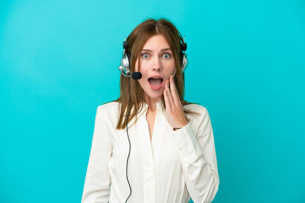 Telemarketer Angol nő dolgozik egy headset elszigetelt kék háttér meglepetés és sokkos arckifejezés - Fotó, kép