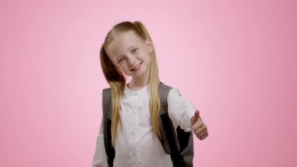 Отличная школа. Милая маленькая школьница с хвостиком и рюкзаком показывая большой палец вверх жестом обеими руками, наслаждаясь образованием, розовый студийный фон, замедленная съемка - Кадры, видео