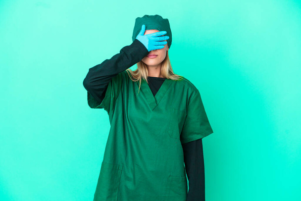 Jeune chirurgien uruguayenne en uniforme vert isolé sur fond bleu couvrant les yeux par les mains. Je ne veux pas voir quelque chose - Photo, image